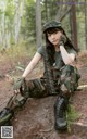 A woman in camouflage sitting on the ground in the woods.