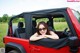 A woman sitting in the driver's seat of a red jeep.