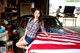 A woman sitting on top of a car with an American flag.