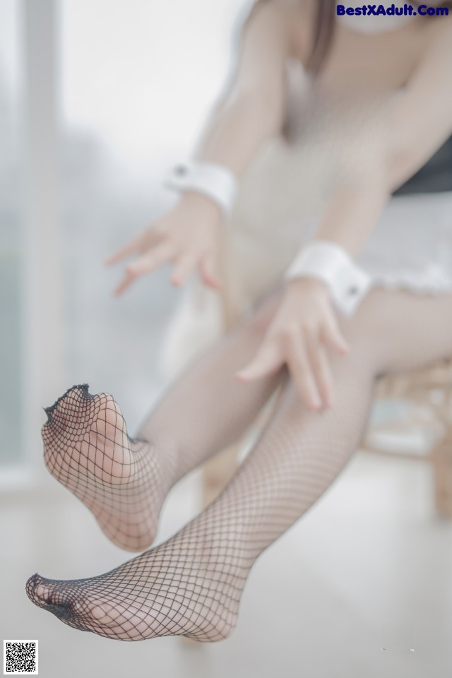 A woman in fishnet stockings sitting on a chair.