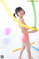 A young girl in a pink bathing suit holding a bunch of balloons.