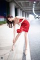 A woman in a red dress leaning against a wall.