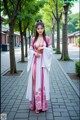 A woman in a pink and white dress standing on a sidewalk.