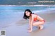 A woman in a red bikini crouching on the beach.