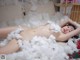 A naked woman laying on top of a bed covered in white cotton.