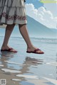 A woman walking on a beach with her feet in sandals.