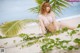 A woman in a bikini sitting on a beach next to a palm tree.