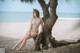 A woman in a bikini sitting on a tree on the beach.