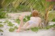 A woman in a bikini laying on the sand under a palm tree.