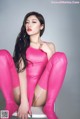 A woman in a pink bodysuit sitting on a white chair.