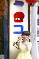 A little girl in a yellow dress standing in front of a sign.