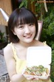 A woman in a yellow dress holding a box of food.