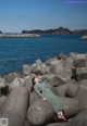 A woman in a green dress sitting on a rock by the ocean.