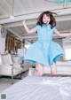 A woman in a blue dress jumping on a bed.