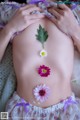 A pregnant woman laying on a bed with flowers on her belly.