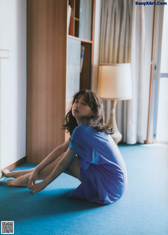 A woman in a blue dress sitting on the floor.