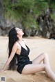 A woman in a black dress sitting on a sandy beach.