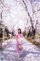 A woman in a pink dress is walking down a path with cherry blossoms.