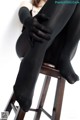 A woman sitting on top of a wooden chair wearing black tights.