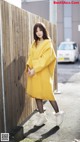 A woman in a yellow coat leaning against a wooden fence.