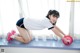 A woman in a white shirt and blue shorts doing push ups with a red ball.