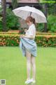 A woman standing in the grass holding an umbrella.